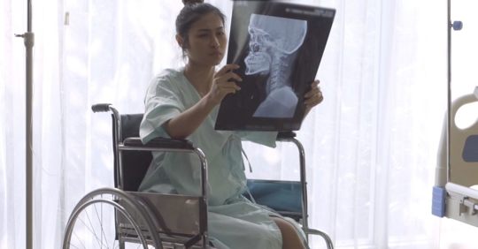 young woman sitting in a wheelchair looking at a head and neck x-ray