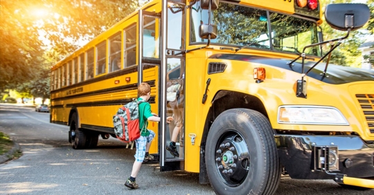 close up of a young boy wearing a backpack and stepping into a school bus